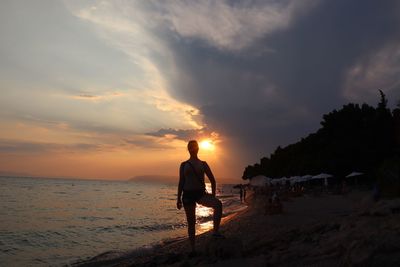 Silhouette woman standing at beach against sky during sunset