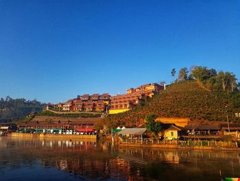 Buildings by river against clear blue sky