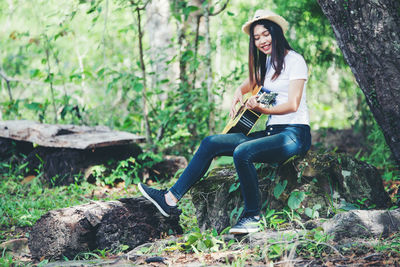 Full length of young woman sitting on tree