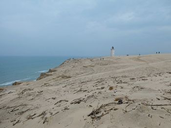 Scenic view of sand dune against sky with rudbjerg knude lighthouse in the background.