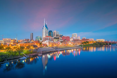 Reflection of illuminated buildings in river against blue sky