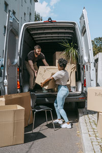 Multiracial couple unloading cardboard boxes from van trunk