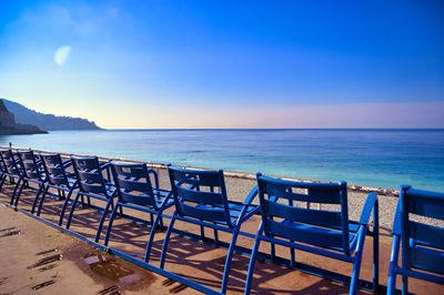 Empty chairs and table at beach against blue sky