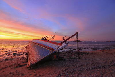 Fishing boat on beach against sky during sunset