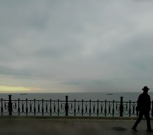 Silhouette men on railing by sea against sky