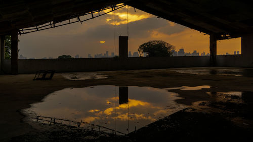 Reflection of silhouette buildings on puddle against sky during sunset