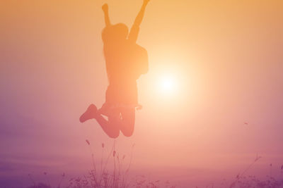 Silhouette person jumping against sky during sunset