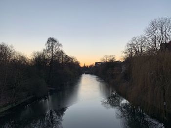 Canal amidst trees against clear sky during sunset