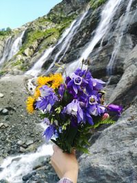 Cropped hand of woman holding bouquet against waterfall