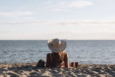 Rear view of woman wearing hat lying at beach against sky