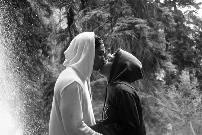 Side view of man and woman standing by tree in forest