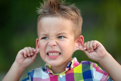 Close-up of cute boy clenching teeth while pulling ears outdoors