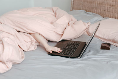 Bored funny child lying in bed under blanket and learning in virtual online school. hands typing