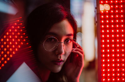 Portrait of young woman standing against illuminated city at night