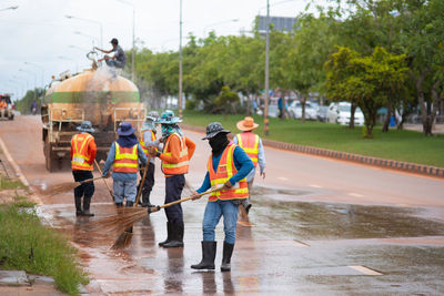 Rear view of sweepers cleaning road against sky