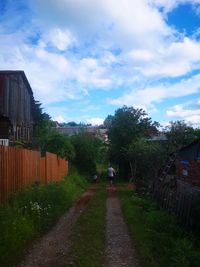 Road amidst trees and houses against sky