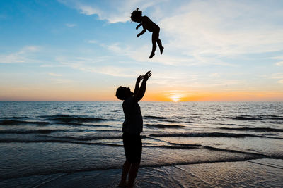 Father throws his daughter into the air at sunset on beach vacation