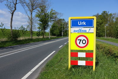 Road sign by trees against sky