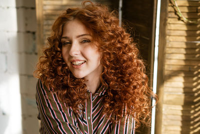 Portrait of happy redhead young woman near window
