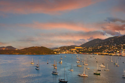 Sailboats moored in sea against sky during sunset