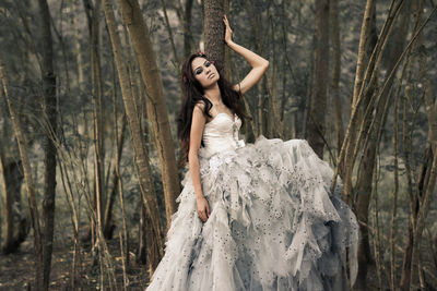 Portrait of female model in white evening gown posing by trees