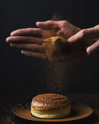 Cropped hands garnishing dessert against black background