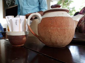 Close-up of coffee pot by sugar packets in bowl on table