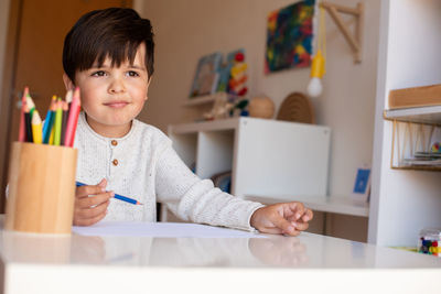 Cute boy holding colored pencil at home