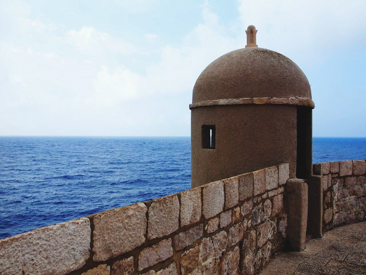 sea, horizon over water, built structure, architecture, water, building exterior, lighthouse, sky, blue, tranquil scene, guidance, tranquility, protection, scenics, day, nature, outdoors, beauty in nature, safety, rock - object