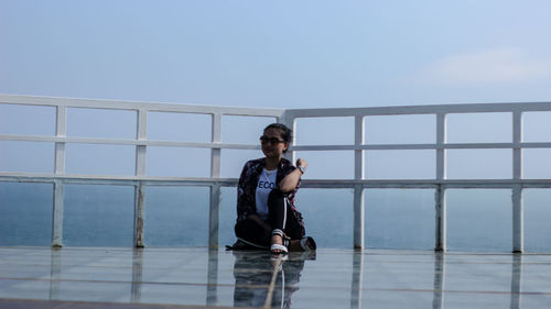 Portrait of man sitting on railing against sea