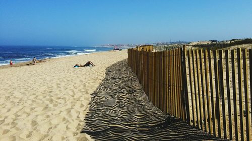 Wooden railing at beach against clear blue sky