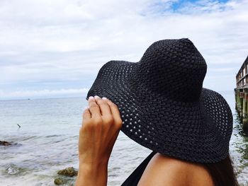 Close-up of woman wearing black hat on beach against sky