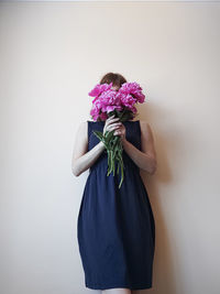 Midsection of woman with bouquet against wall