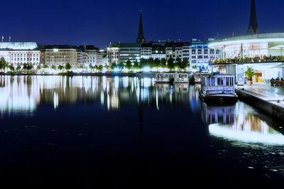 Boat moored at binnenalster lake by illuminated cityscape at night