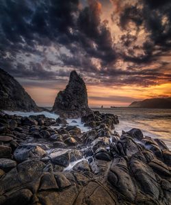 Rocks on beach against sky during sunset