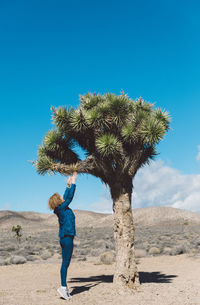 Woman standing by tree against blue sky