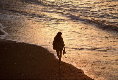 Rear view of man walking on beach during sunset