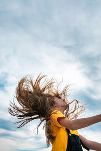 Side view from below of peaceful teenager throwing long hair on background of cloudy sky in summer
