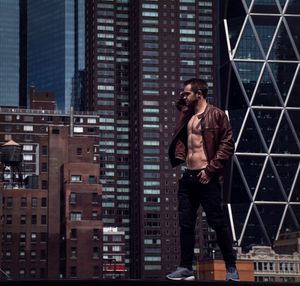 Full length portrait of young man standing against buildings in city