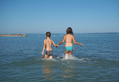 Siblings wading in sea against clear sky