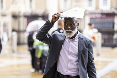 Senior businessman covering head with newspaper on rainy day