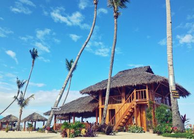 Palm trees growing by traditional building at beach against sky