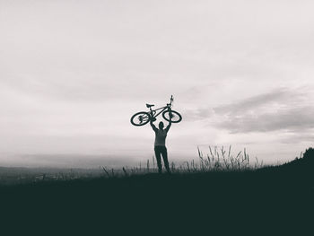 Rear view of man holding bicycle on field against sky