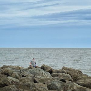 People sitting on rock by sea against sky