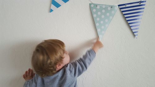 Rear view of baby boy playing with flags on wall at home