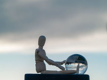 Close-up of figurine with crystal ball against cloudy sky