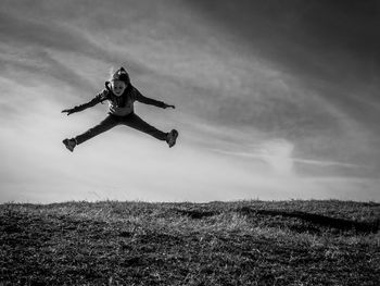 Girl jumping mid-air over grass against sky