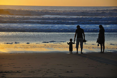 Parents with son standing at beach during sunset