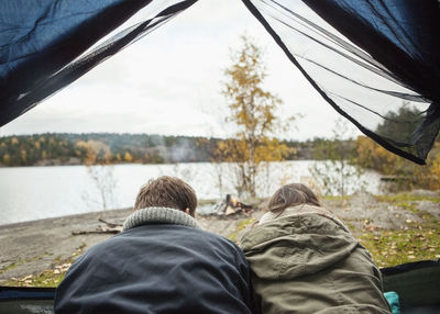 Rear view of couple lying in tent at lakeshore