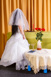 Jewish bride in a white dress, veiled face, stands with her back in front of the chupa ceremony